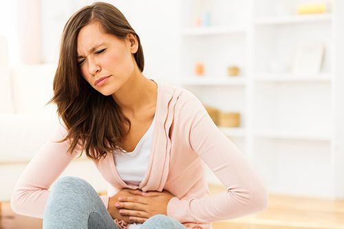 mujer joven con las manos en la barriga con gesto de dolor