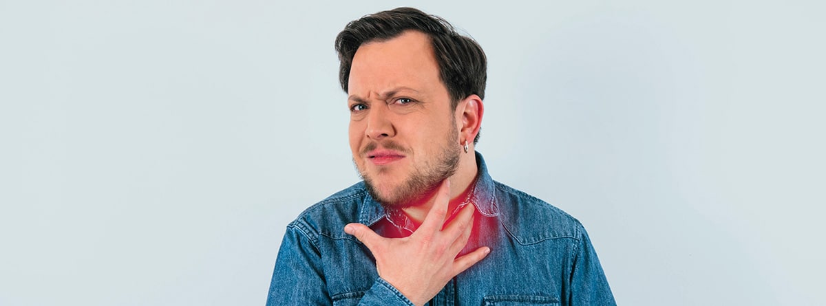 Disfonía y afonía, causas y tratamiento: hombre con la mano en el cuello enrojecido, con actitud de dolor