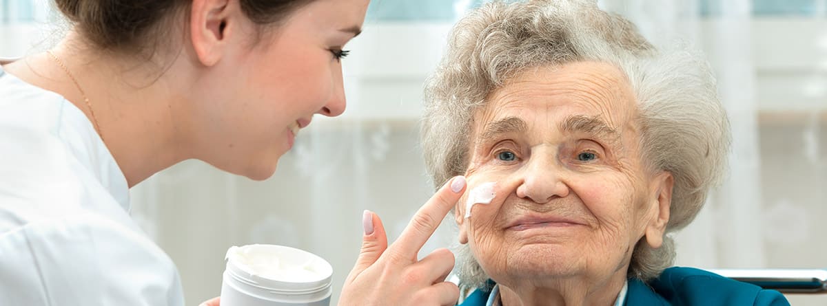 Prevención de enfermedades de la piel en personas mayores: Enfermera asiste a una anciana con medidas de higiene y cuidado de la piel en casa