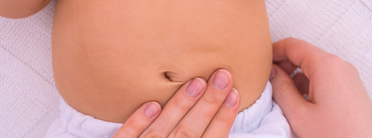 Bebé con la tripa hinchada y mano de mujer dando un masaje