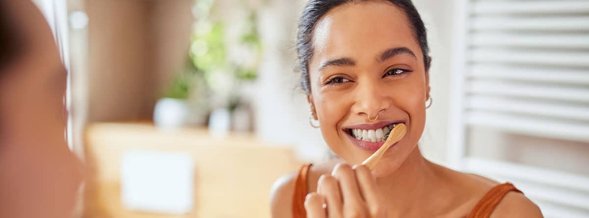 Mujer joven sonriente cepillándose los dientes en el baño.