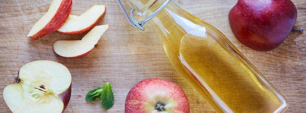 Botella de vinagre de manzanas con varias manzanas rojas alrededor.
