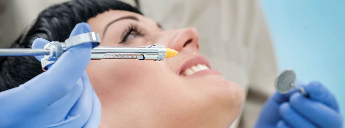 Mujer sonriente en la camilla del dentista, con un jeringuilla cerca de la boca